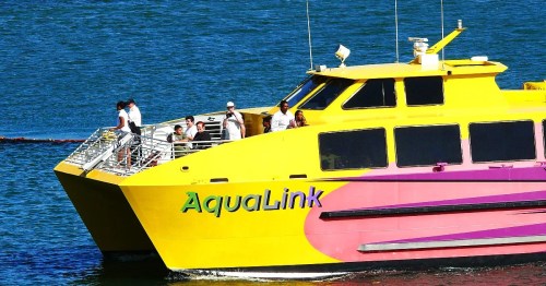 A bright yellow ferry named AquaLink with passengers on board, sailing on blue water.