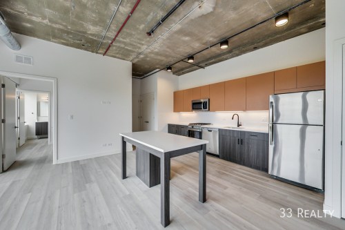 Modern kitchen and living area with a concrete ceiling, sleek cabinets, and a central island. Bright and spacious layout.