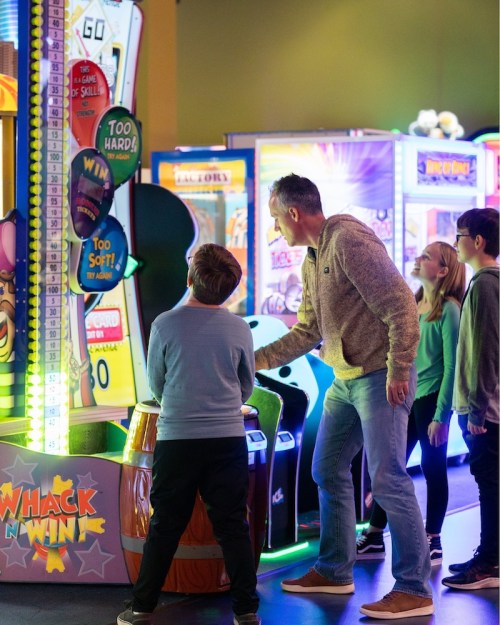 A man and children play an arcade game called "Whack N Win" in a colorful game room.
