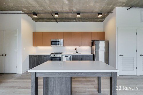 Modern kitchen with a large island, stainless steel appliances, and sleek cabinetry under a concrete ceiling.