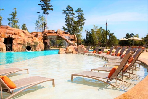 A serene pool area with lounge chairs, a water slide, and lush greenery in the background under a clear blue sky.