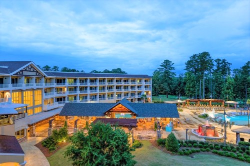 A scenic view of a hotel with a pool area, surrounded by greenery and a cloudy sky at dusk.