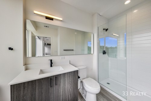 Modern bathroom featuring a sleek vanity, large mirror, and a glass shower enclosure. Bright and minimalist design.