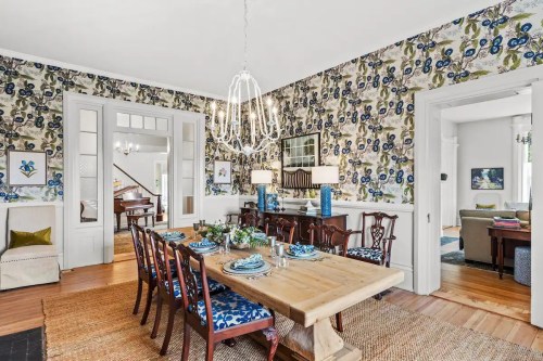 A stylish dining room with a wooden table, floral wallpaper, and elegant lighting, featuring a cozy atmosphere.