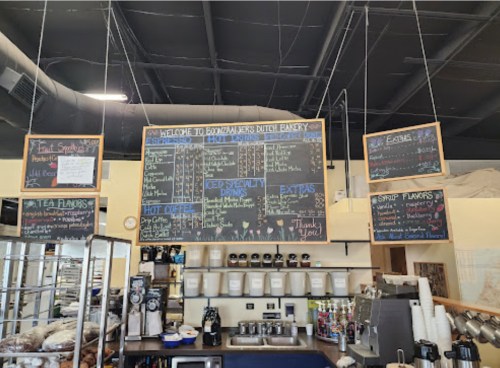 Menu board at a bakery featuring various drinks, pastries, and specialty items, with prices listed.