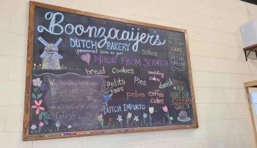 Chalkboard menu at Boonzaaijers Dutch Bakery featuring cakes, bread, cookies, and custom orders. Colorful, hand-drawn design.