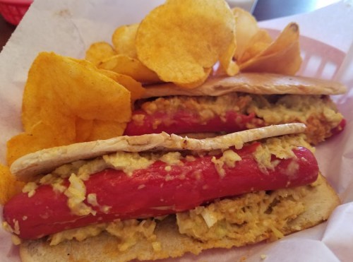 A plate featuring two hot dogs in a bun, topped with a creamy yellow sauce, accompanied by potato chips.