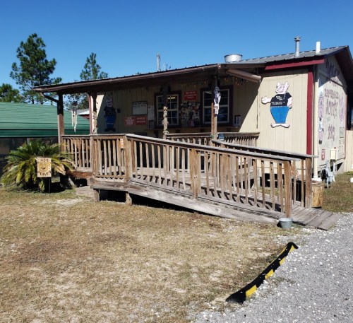 A wooden building with a ramp, featuring signs and decorations, set in a grassy area under a clear blue sky.