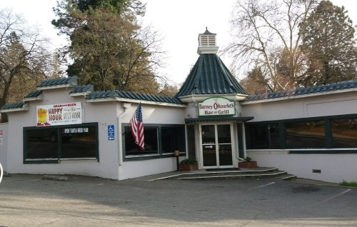 Exterior of Barney O'Rourke's Bar & Grill, featuring a green roof and an American flag, surrounded by trees.