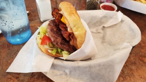 A juicy burger with bacon, lettuce, tomato, and cheese, served in a basket lined with paper.