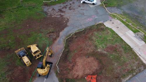 Aerial view of a construction site with heavy machinery, a vehicle, and marked ground areas.