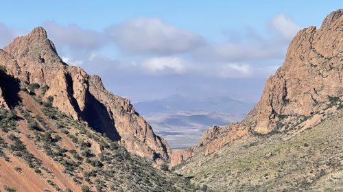 A scenic view of rugged mountains and a valley under a partly cloudy sky.