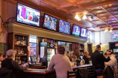 A lively bar scene with multiple TVs showing sports, patrons at the bar, and a well-stocked drink counter.