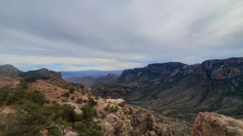 A panoramic view of rugged mountains and valleys under a cloudy sky, showcasing natural beauty and vast landscapes.