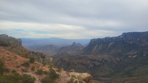 A panoramic view of rugged mountains and valleys under a cloudy sky, showcasing natural beauty and vast landscapes.
