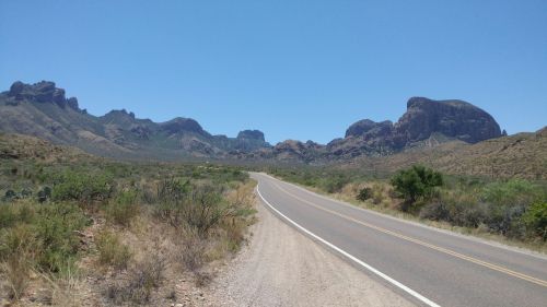 A winding road leads through a desert landscape with rugged mountains under a clear blue sky.