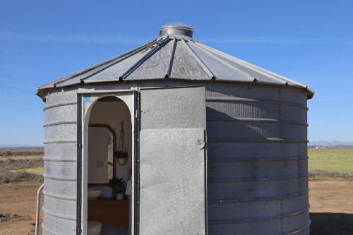 A round metal structure with a door, set in an open field under a clear blue sky.