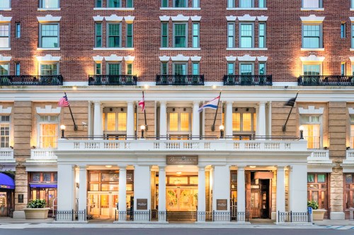 Historic hotel facade with brick exterior, large entrance, and flags displayed, illuminated at dusk.