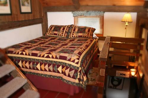 Cozy bedroom with a quilted bedspread, wooden beams, and a warm lamp, featuring a staircase and rustic decor.