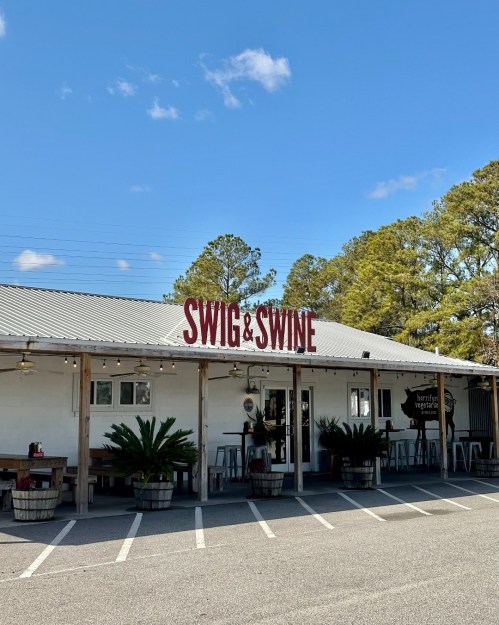 Exterior of a restaurant named "Swig & Swine," featuring a rustic design and surrounded by greenery.