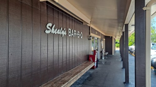 Exterior view of Shady Bar-B-Q with a wooden bench and signage, set in a casual dining area.