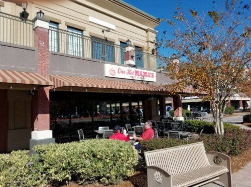 Exterior of a restaurant named "One Hot Mama's," featuring outdoor seating and a clear blue sky.
