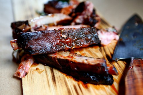 Close-up of smoked ribs with a rich glaze, resting on a wooden cutting board next to a knife.