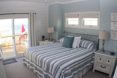 Cozy beachside bedroom with a striped bedspread, lamps, and a view of the ocean through sliding glass doors.