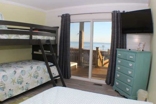 Cozy bedroom with bunk beds, a turquoise dresser, and a view of the beach through sliding glass doors.