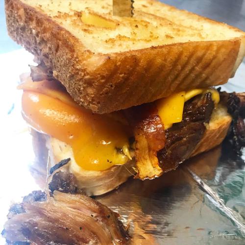 A close-up of a grilled sandwich with melted cheese, bacon, and meat, served on toasted bread.