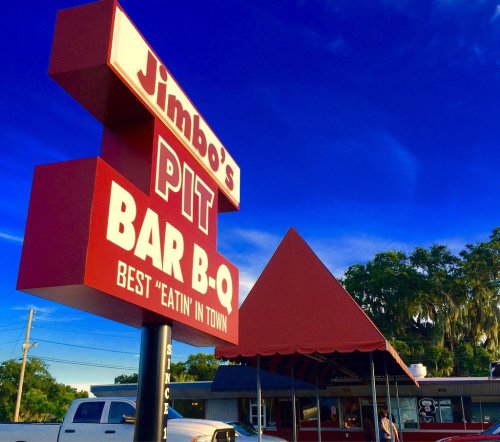 Sign for Jimbo's Pit Bar-B-Q with a blue sky and trees in the background, promoting "Best 'Eatin' in Town."