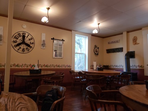 Cozy dining area with wooden tables, chairs, a clock, and decorative wall accents in warm tones.