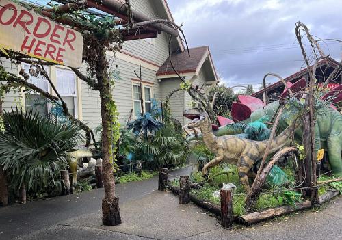 A whimsical outdoor display featuring colorful dinosaur sculptures surrounded by greenery and a sign that says "Order Here."