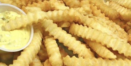 A close-up of golden crinkle-cut fries served with a small bowl of dipping sauce.
