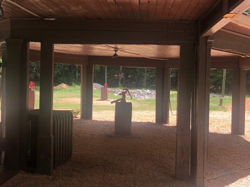 A covered outdoor area with wooden beams, featuring a central pedestal and targets in the background.