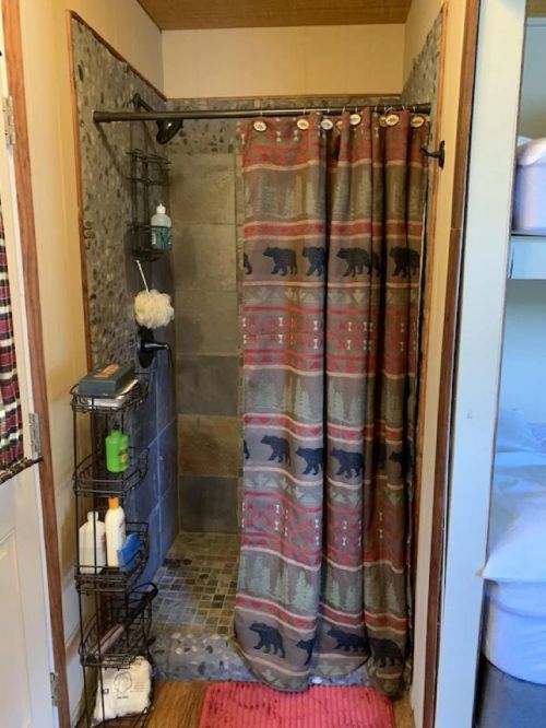 A rustic shower with a patterned curtain, stone walls, and shelves for toiletries in a cozy bathroom setting.