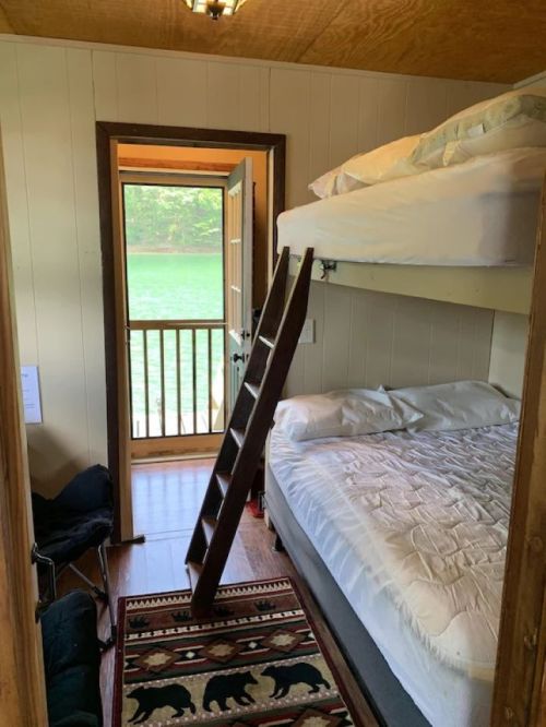 Cozy cabin interior with a bunk bed, a double bed, and a view of a lake through an open door.