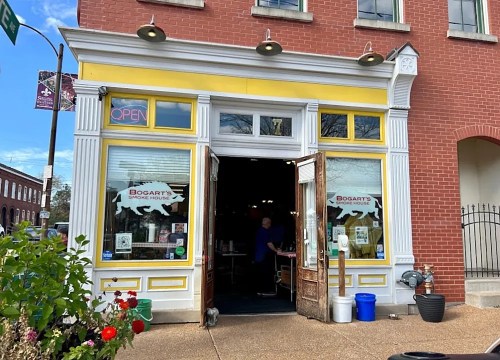 A vibrant storefront of Bogart's Smoke House, featuring an open door and colorful flowers in front.