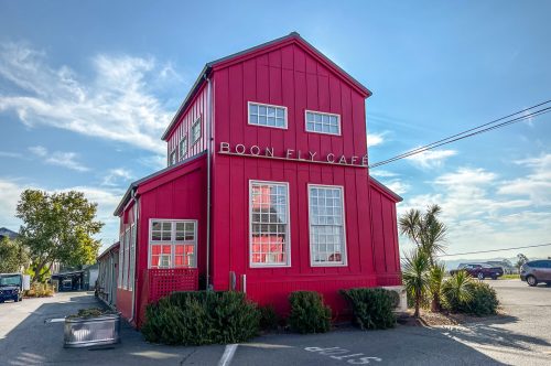 A bright red building with large windows, labeled "Boon Fly Café," set against a clear blue sky.