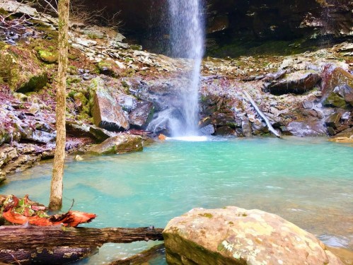 A serene waterfall cascades into a turquoise pool, surrounded by rocky terrain and lush greenery.