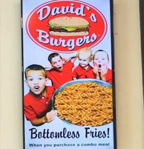 A colorful sign for David's Burgers featuring excited kids and a large bowl of fries, promoting bottomless fries with a combo meal.