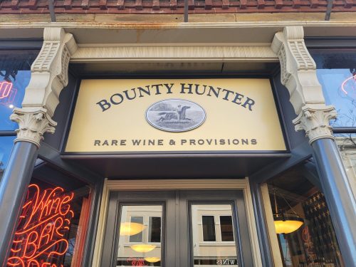 Sign for "Bounty Hunter Rare Wine & Provisions" on a storefront, featuring decorative architectural details.