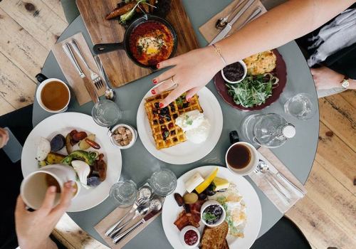 A table set with various breakfast dishes, including waffles, eggs, and fruits, with hands reaching for food.