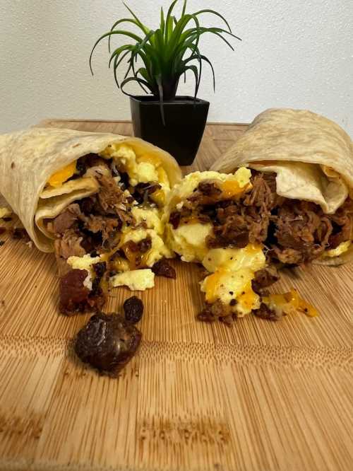 Two burritos filled with beef, scrambled eggs, and cheese, partially opened on a wooden surface, with a small plant in the background.