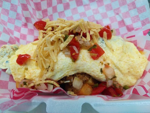 A delicious omelet topped with diced tomatoes, crispy onions, and herbs, served in a pink checkered container.