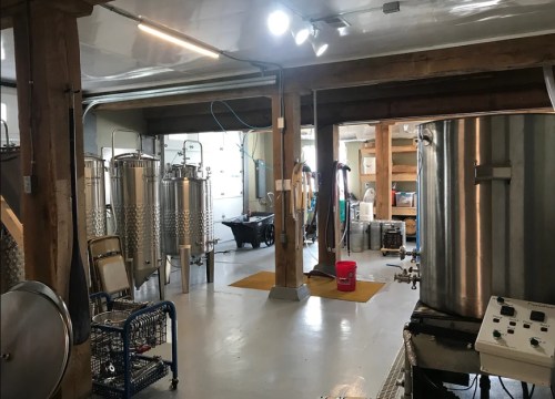 Interior of a brewery with stainless steel tanks, brewing equipment, and a clean, organized workspace.
