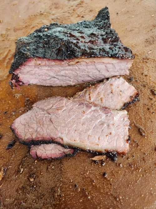 Sliced smoked brisket on a wooden cutting board, showcasing a smoky crust and tender pink interior.