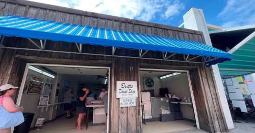 A wooden storefront with blue-striped awning, featuring a sign for Britt's Donut Shop and customers inside.