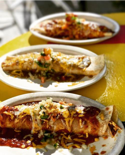 Three plates of enchiladas topped with cheese, sauce, and fresh toppings, served on a colorful table.