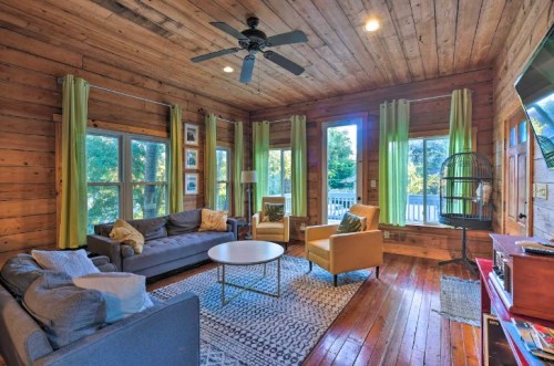 Cozy living room with wooden walls, large windows, green curtains, a coffee table, and comfortable seating.